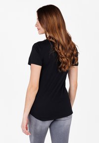 Camiseta de algodón negra con mangas cortas, diseño ajustado y dobladillo redondeado. Combinada con jeans grises, mostrando un estilo casual y sencillo.