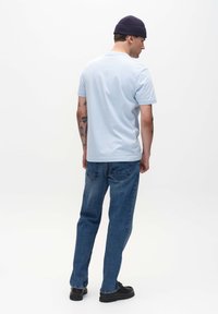 Svetlomodré tričko s krátkym rukávom v kombinácii s modrými džínami. Tričko má okrúhly výstrih; slim fit denim pôsobí mierne opotrebovane a má vrecká.