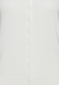 Bílý pletený kardigan se sedmi malými bílými knoflíky vertikálně uspořádanými po středu předku.