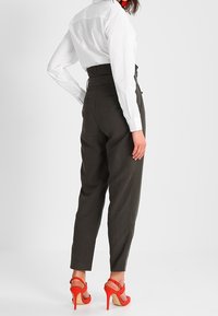 Ciemnoszare spodnie o wysokim stanie i zwężanym kroju, połączone z białą koszulą zapinaną na guziki oraz czerwonymi sandałami na obcasie.