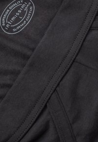 Černá bavlněná tkanina s hladkým povrchem, obsahující prošitý šev a štítek označující 'Superior Quality' a 'Supima Cotton'.