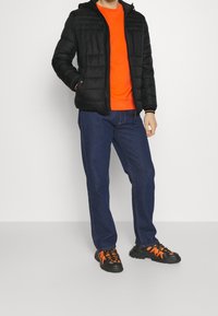 Czarna kurtka puchowa, pomarańczowa bluza, niebieskie dżinsy i czarne tenisówki z pomarańczowymi akcentami. Posiada zamek błyskawiczny i prążkowane mankiety.