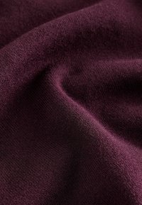 Tejido de punto burdeos que muestra una superficie suave y texturizada con un ligero brillo, exhibiendo una elasticidad moderada y un patrón de tejido uniforme.