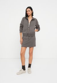 Γκρι φούτερ με φερμουάρ και ριμπ μανσέτες, συνδυασμένο με μια mini φούστα στο ίδιο χρώμα. Αθλητικά παπούτσια και σκούρες κάλτσες ολοκληρώνουν την εμφάνιση.