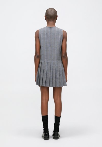 Pelēkā pārlieku apģērba kleita ar plisētu svārku, bez piedurknēm un aizmugurējo rāvējslēdzēju. Modelis valkā melnas līdz ceļiem zeķes un kurpes.