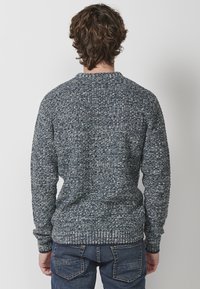 Su�éter de punto en azul marino y gris, con un patrón texturizado, cuello redondo y puños de canalé. Combinado con pantalones de mezclilla azules.