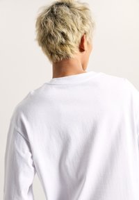 Weißes Baumwoll-T-Shirt mit langen Ärmeln und klassischem Rundhalsausschnitt. Glatte Textur, lockere Passform und schlichtes Design ohne zusätzliche Muster oder Akzente.