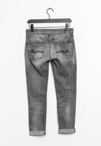 Grå denimjeans med lätt slitning, med två bakfickor med vågformad söm och uppvikta cuffs. Hänger från en svart krok.