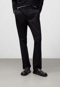 Pantaloni di cotone neri con un design dritto e slanciato, caratterizzati da tasche laterali, passanti per la cintura e una finitura liscia. Abbinati a scarpe nere.
