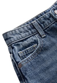 Gros plan sur un jean en denim bleu montrant la poche avant, la petite poche, la passants de ceinture et le rivet métallique sur fond blanc.
