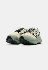 Green and cream running shoes with textured fabric upper, black accents, and Vibram outsole. Features lacing system and protective toe design.