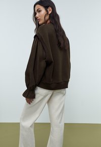 Felpa marrone oversize con maniche a sbuffo, colletto e polsini a costine, abbinata a pantaloni a gamba larga color crema. Design semplice, texture morbida.