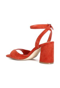 Sandaali avatud varbaga, oranžast seemisnahast, millel on pahkluu rihm ja paks konts. Esiosas on lõikega disain ja sile sisemus.