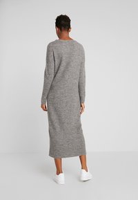 Grå stickad maxiklänning med långa ärmar, rund halsringning och ribbad nederkant, i kombination med vita sneakers. Mjuk textur och löst fall.