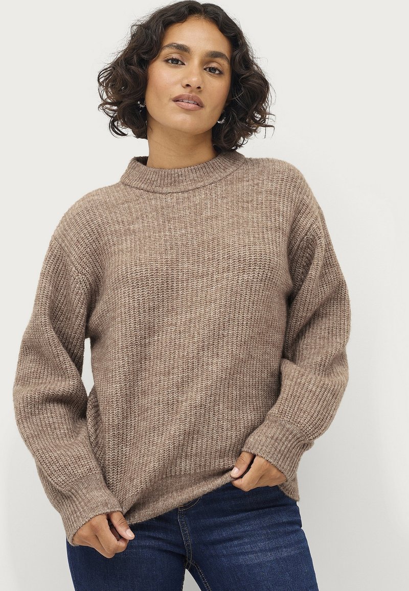 Maglione lavorato a maglia color marrone chiaro con collo alto e spalle scese, caratterizzato da un motivo testurizzato e polsini a costine. Abbinato a jeans scuri.