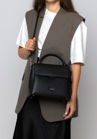 Schwarze Lederhandtasche mit strukturiertem Design, Obergriff und abnehmbarem Tragegurt. Verfügt über einen magnetischen Verschluss und Metallfüße am Boden.