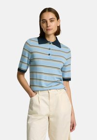 Randig kortärmad polo i ljusblått med marinblå krage och manschetter, med tre knappar och en mjuk textur. Matchad med krämfärgade byxor.