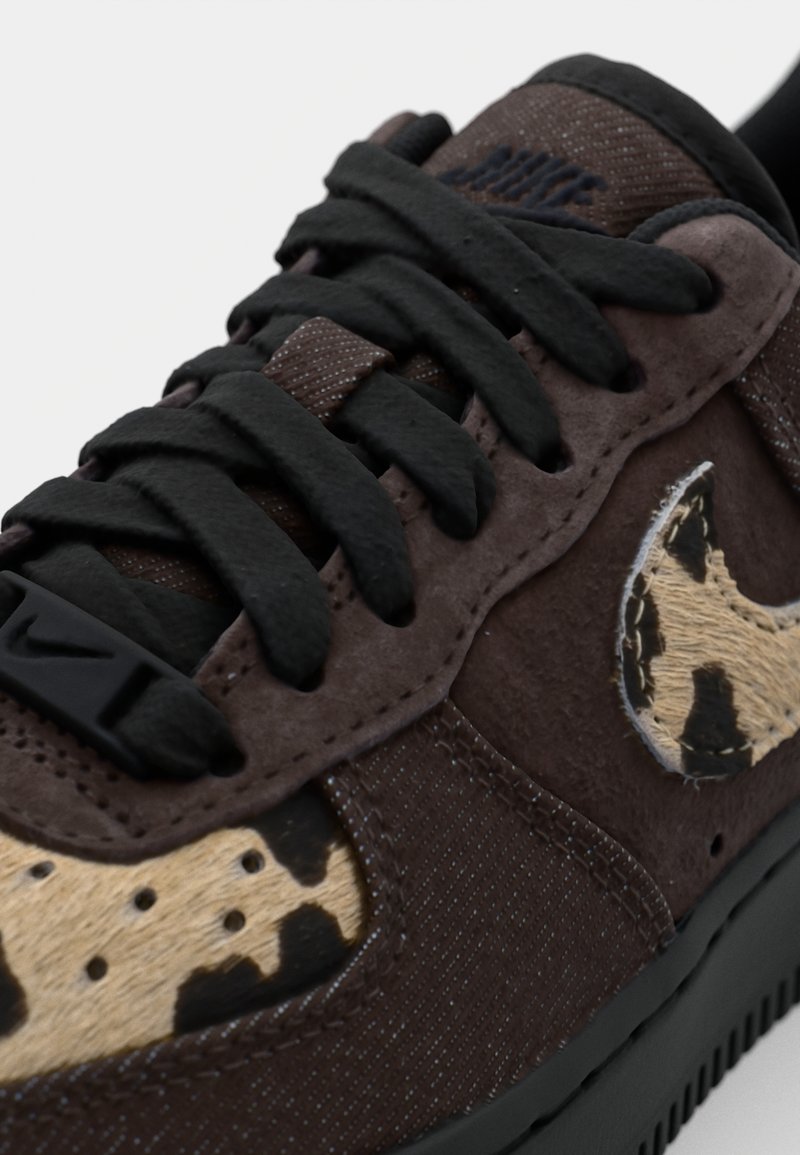 Braune Wildledersneaker mit schwarzen Schnürsenkeln, die ein tan- und schwarz gepunktetes Design an der Seite und eine strukturierte, dunkle Sole aufweisen.