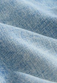 Mėlynas džinso audinys su minkštu, tekstūruotu pynimu, pasižymintis klasikinio slubo raštu. Spalva yra šviesiai, išblukusiai mėlyna.