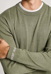 Olivgrüner Strickpullover mit Rundhalsausschnitt und gerippten Bündchen. Mit dezentem "Pepe Jeans"-Logo auf dem linken Ärmel. Weiche Textur.