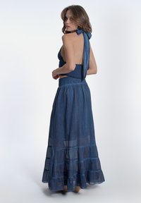 Abito lungo e fluente di colore blu con scollatura a collo alto, corpino arricciato, balze sovrapposte all'orlo e una texture leggera e trasparente.