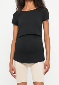 Svart graviditetst-shirt med rundad nederkant och korta ärmar, parat med ljusbeiga cykelbyxor, tillverkade av mjukt, elastiskt tyg.