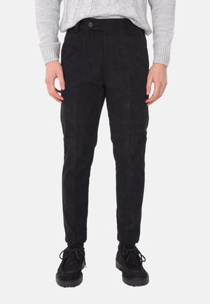 Pantaloni in corduroy neri con vestibilità dritta, dotati di chiusura con bottone e tasche laterali. Indossati con un maglione grigio a trecce e scarpe nere.
