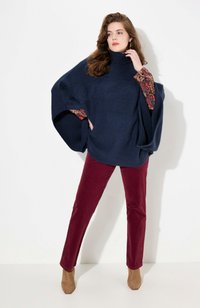 Un pull-over turtleneck en tricot surdimensionné navy avec des manches à motifs, associé à un pantalon en velours côtelé bordeaux et des bottines camel.
