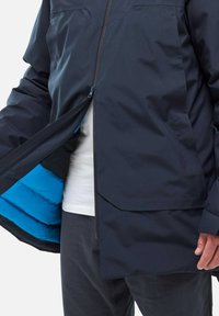 Marineblaue wasserdichte Jacke mit Reißverschluss vorne, ausgestattet mit einem tealfarbenen isolierten Innenfutter und einem lockeren Schnitt. Texturiertes Material, geeignet für kühleres Wetter.