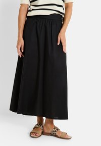 Falda midi negra con una cinturilla fruncida, hecha de un tejido liviano. Combinada con sandalias destalonadas de estampado de leopardo y una blusa de rayas.