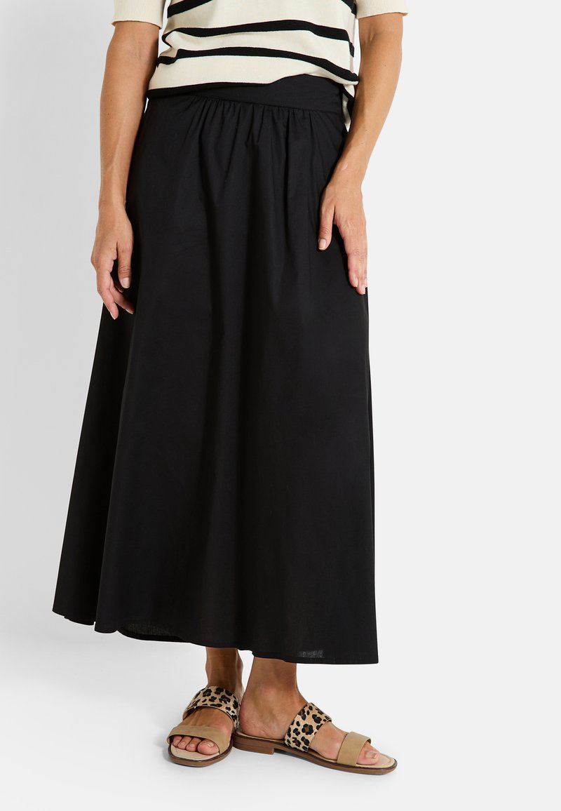 Falda midi negra con una cinturilla fruncida, hecha de un tejido liviano. Combinada con sandalias destalonadas de estampado de leopardo y una blusa de rayas.