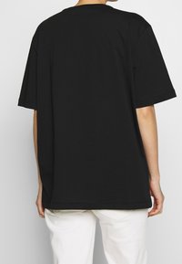 T-shirt nera oversize in cotone, con collo rotondo e maniche corte, dalla texture liscia e dal fit rilassato.