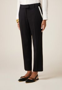 Op maat gemaakte zwarte broek met een rechte pijp, voorzien van een tailleband en zijstrepen. Gemaakt in combinatie met zwart en bruin puntige ballerina's.