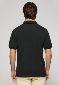 Polo negro con un cuello clásico y mangas cortas, confeccionado en una tela suave con una textura lisa. Vista trasera mostrada.
