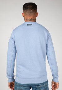 Sudadera de color azul claro hecha de una mezcla de algodón, con cuello redondo, mangas largas y un logo impreso en negro en la parte posterior del cuello.