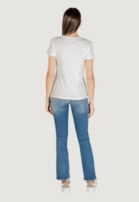 Camiseta de algodón blanca con mangas cortas, ajuste clásico. Combinada con unos jeans de mezclilla acampanados de color azul claro. Vista trasera con líneas limpias y sin logotipos visibles.