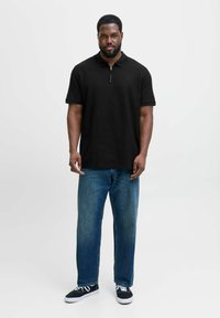 Sort polo-shirt med lynlås krave, parret med lys blå lige jeans og sorte sneakers med hvide snørebånd.