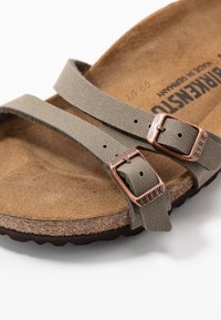 Nærbillede af taupe Birkenstock sandal med to justerbare læderremme og kobberfarvede spænder over korksål.