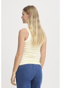 Top de tirantes a rayas en blanco y amarillo, hecho de tela acanalada, con un diseño ajustado. Combinado con jeans de mezclilla azul.