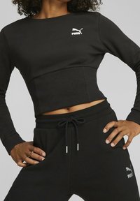 Top a maniche lunghe cropped nero con texture a coste e logo Puma sul petto, abbinato a pantaloni jogger neri con cordino e tasche laterali.
