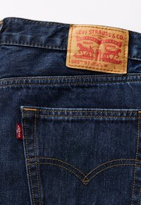 Poche arrière en jean bleu denim avec patch en cuir de marque Levi Strauss & Co. et étiquette en tissu rouge Levi's sur la couture latérale.