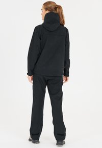 Svart vattentät jacka med huva och justerbara ärmar, tillsammans med matchande löst sittande byxor. Materialet verkar hållbart med en slät textur.