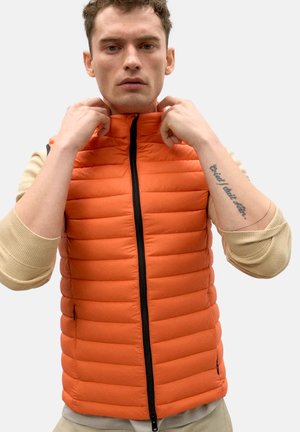 Chaleco acolchado naranja con patrón de costura horizontal, cuello alto y cremallera frontal; mangas largas de una blusa beige visibles debajo.