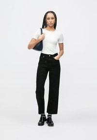 Czarne spodnie z wysokim stanem o prostych nogawkach, zestawione z dopasowaną białą koszulką z krótkim rękawem. Modelka niesie granatową torebkę na ramię.