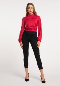 Top roșu din satin cu mâneci lungi, guler înalt și talie strânsă, asortat cu pantaloni negri slim-fit și pantofi cu toc înalt negri.