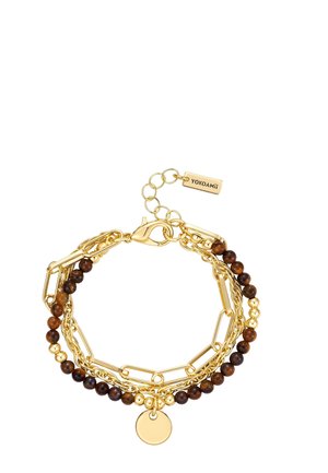 Gelaagde armband in goudkleur met bruine kralen, schakelketting, een ronde hanger en een verstelbare sluiting met een YOKOAMii-label.