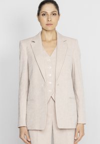 Jasnoróżowy garnitur z lnu, składający się z marynarki zapinanej na jeden guzik, z klapami i dopasowaną kamizelką z ozdobnymi guzikami. Gładka tekstura, dopasowany krój.