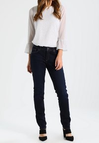 Blusa bianca con pois neri e maniche a campana abbinata a jeans slim-fit blu scuro e scarpe con tacco nere.