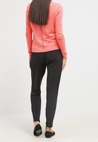 Korallfärgad tröja med långa ärmar och en mittsömm bak, kombinerad med svarta smala byxor och svarta ballerinas. Slät textur är tydlig.