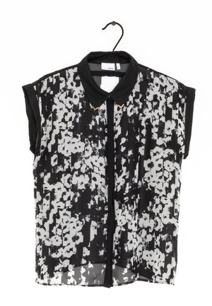 Blouse à manches courtes imprimé floral noir et blanc avec col noir et pointes de col dorées suspendue à un cintre noir.